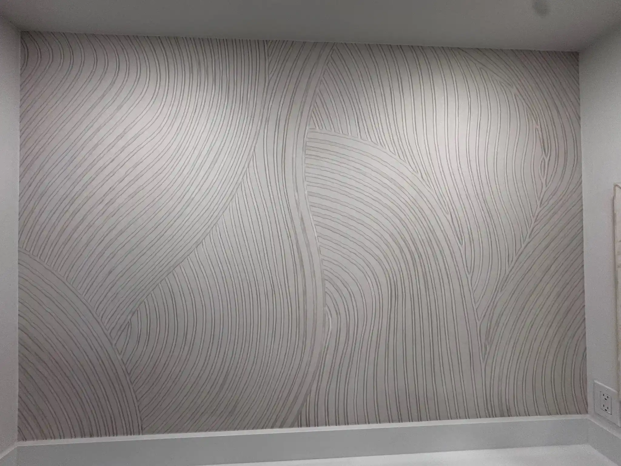 Close view of an ivory wallcovering with a flowing gray line pattern above white trim.