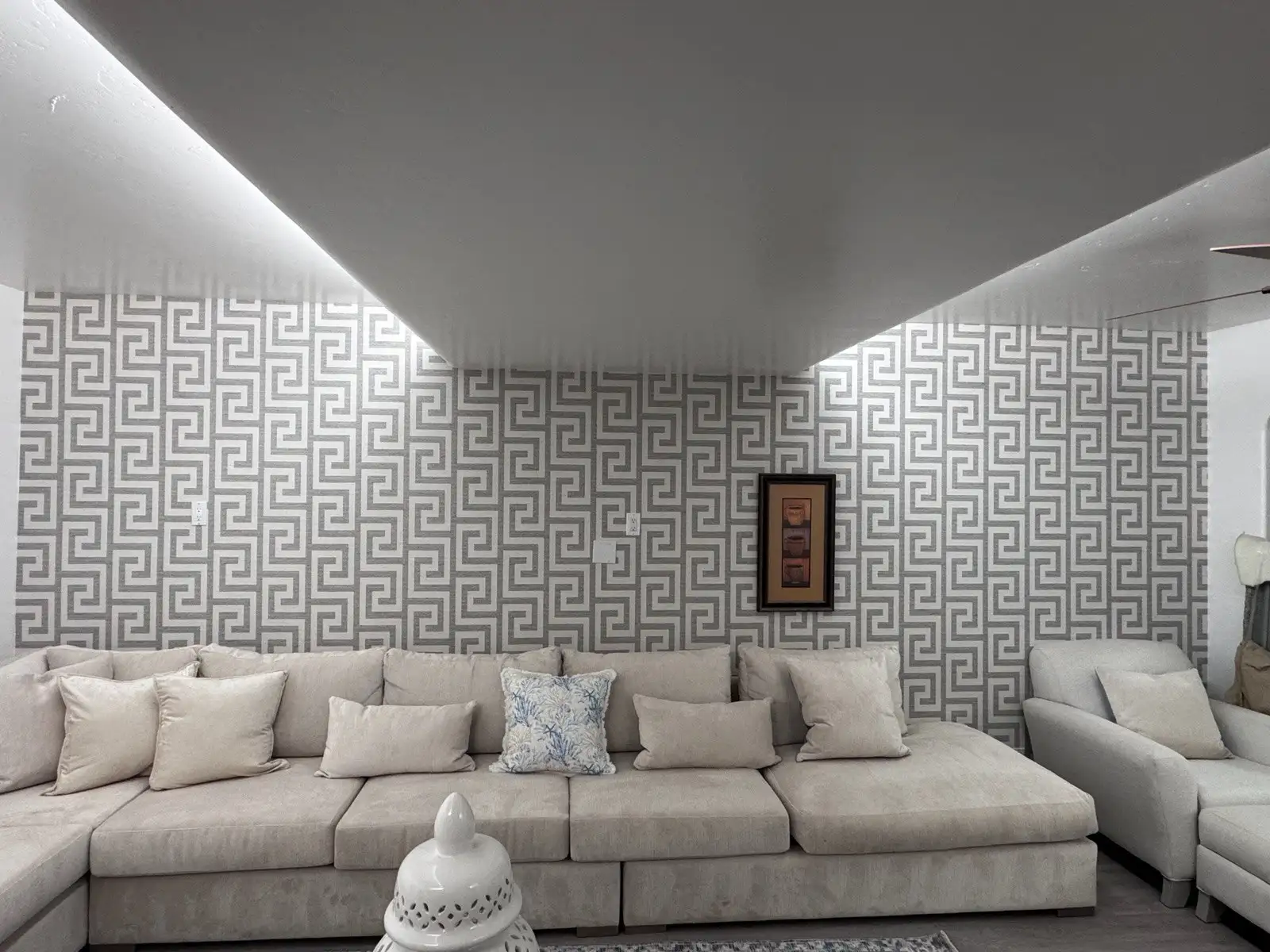 Cream sectional beneath a silver-gray Greek key patterned wallcovering in a modern living room.