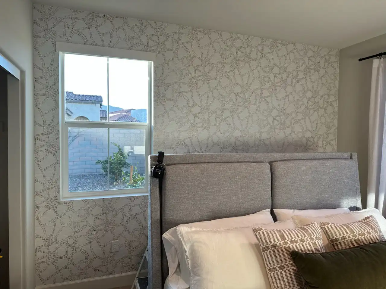 Bedroom with a tall gray upholstered bed and a pale gray abstract patterned accent wall.